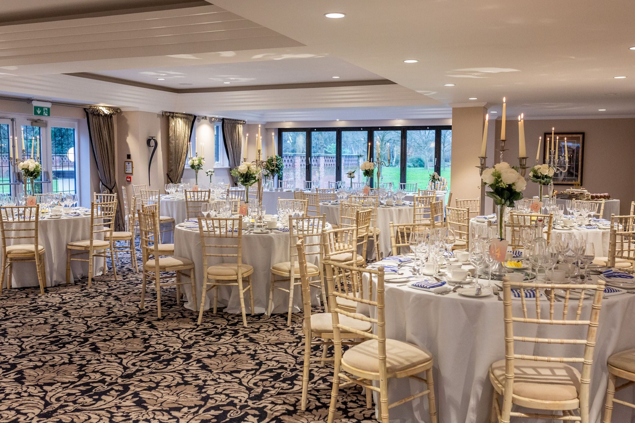 A banquet hall with round tables, white tablecloths, and gold chairs.