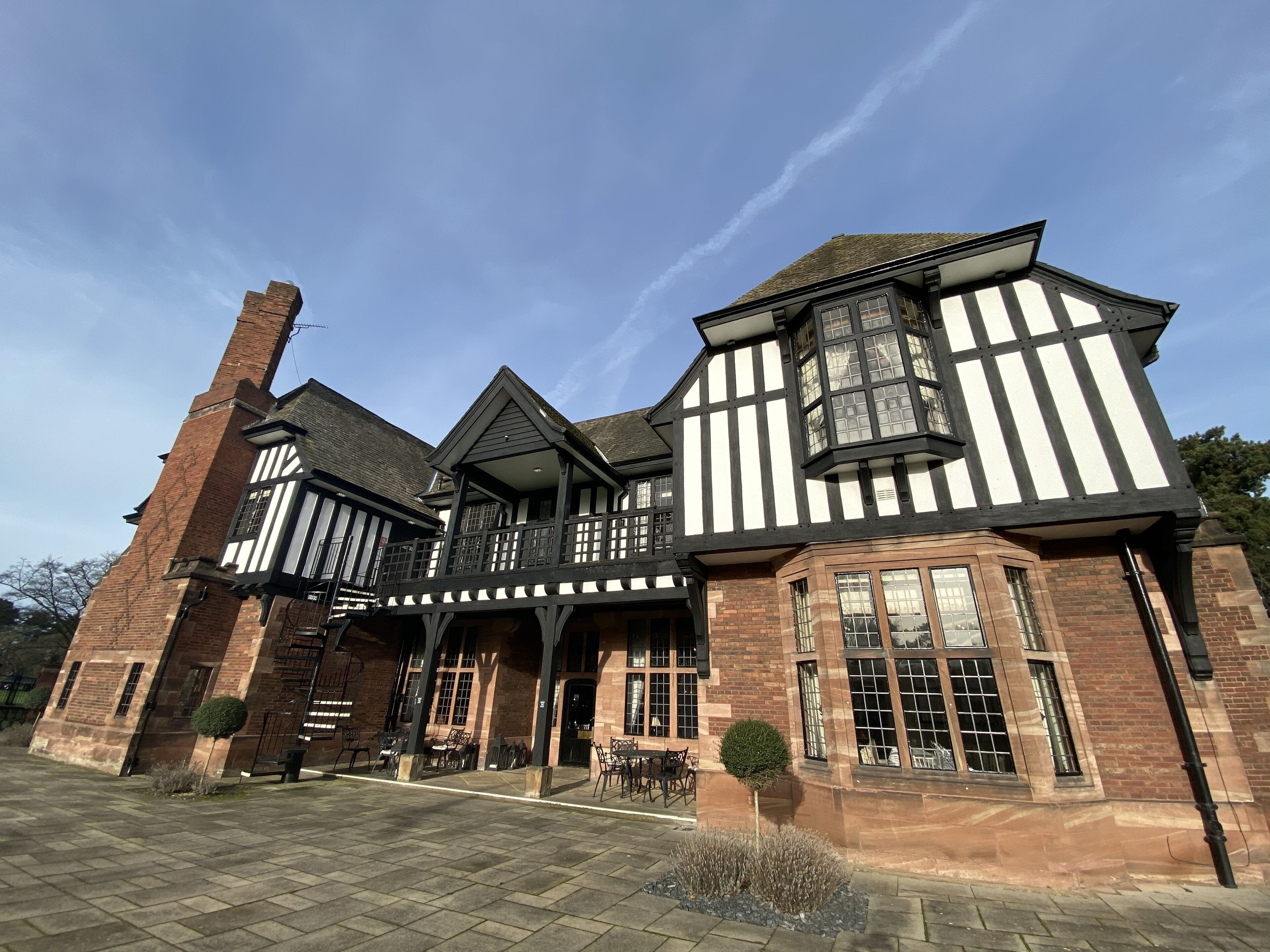 A traditional Tudor-style building with a prominent chimney, large windows, and a balcony with outdoor seating.