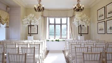 A formal room with rows of chairs, a central aisle, and chandeliers.