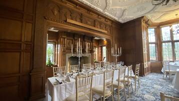 Un comedor formal con una larga mesa dispuesta para una comida, flanqueada por paneles de madera ornamentados y un techo decorativo.