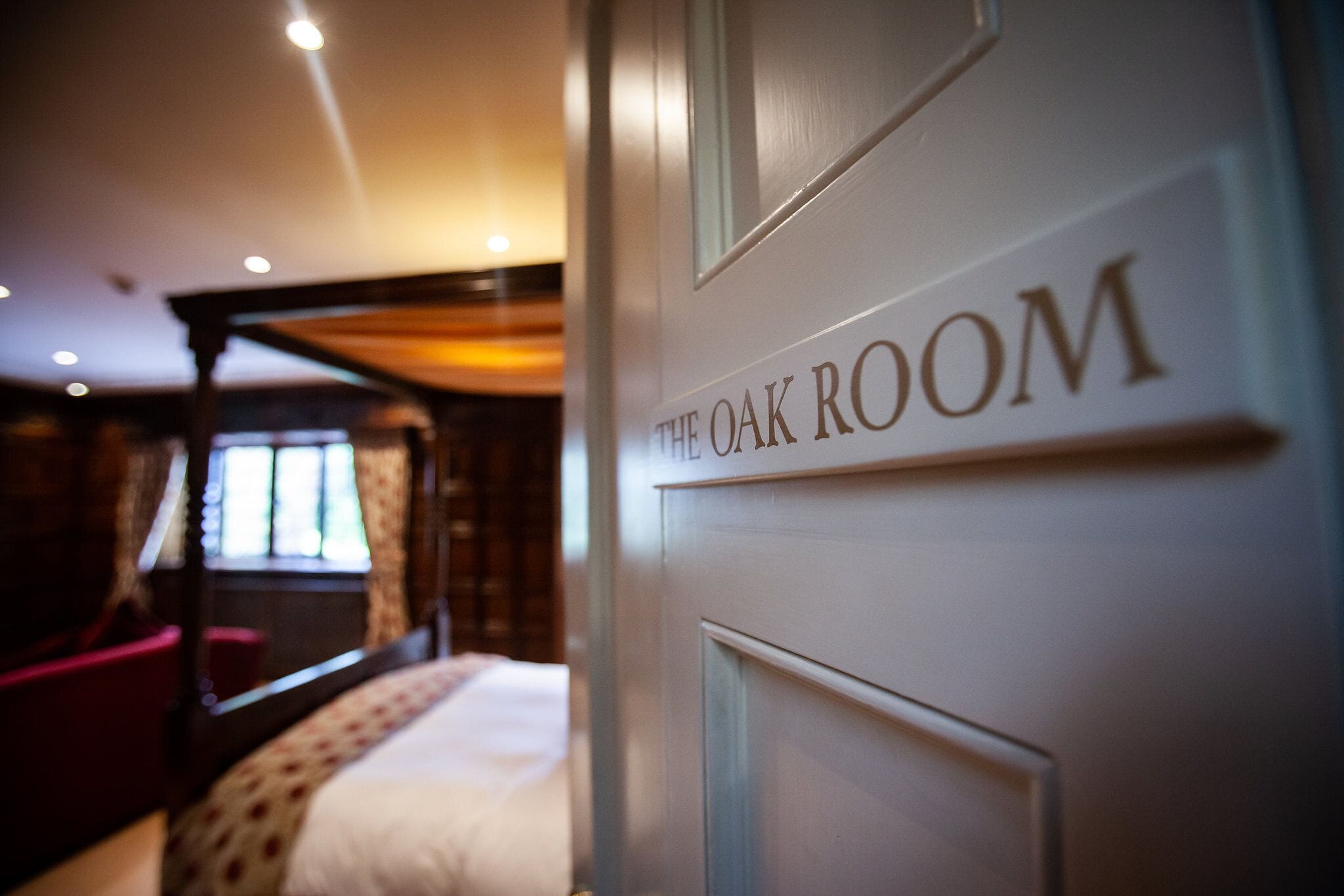 A room with a bed, a red chair, and a sign that reads "The Oak Room".