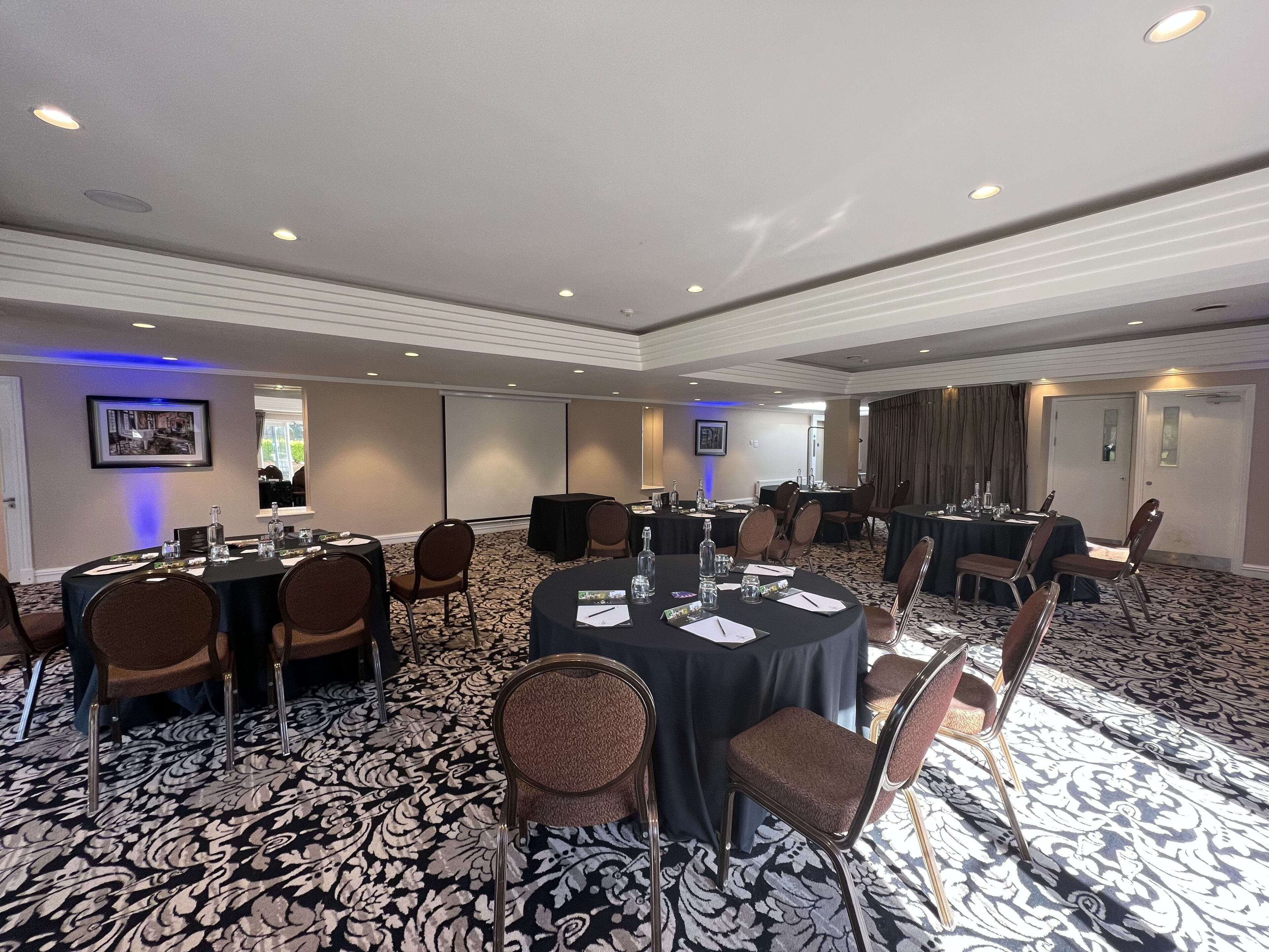 A conference room with round tables, chairs, and a patterned carpet.