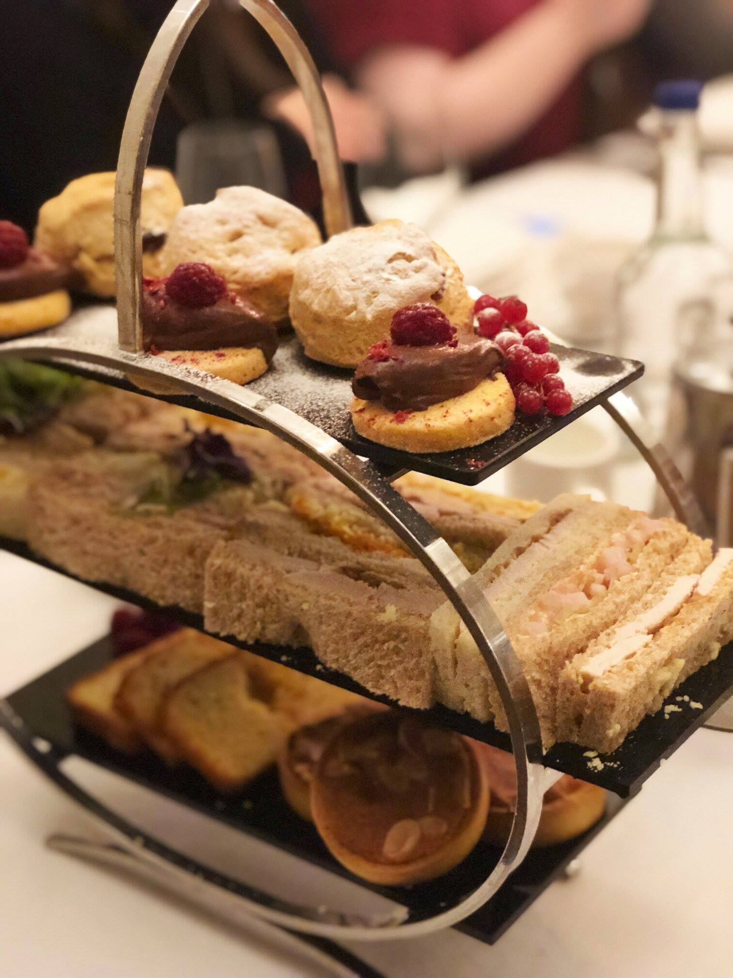 Ein gestaffeltes Tablett mit Sandwiches und Scones, manche mit Beeren und Schokolade.