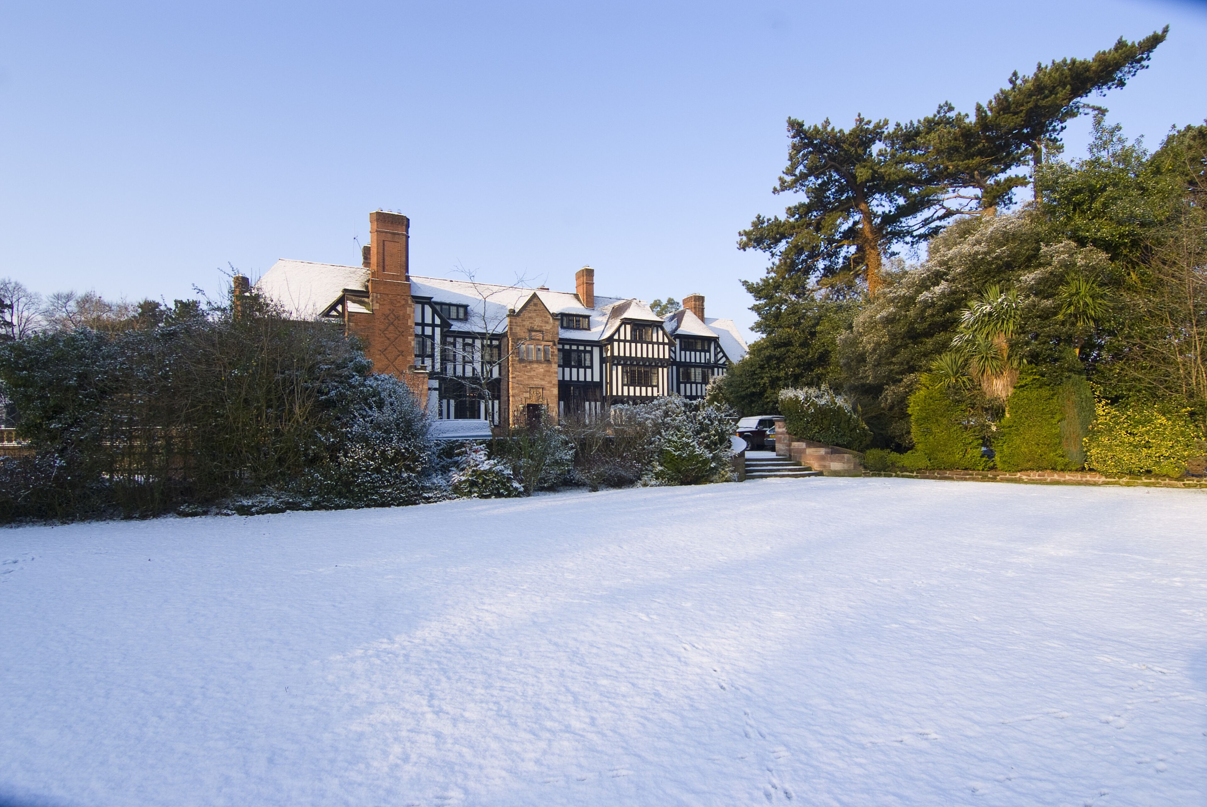 Una casa grande e histórica con un jardín nevado y árboles circundantes.