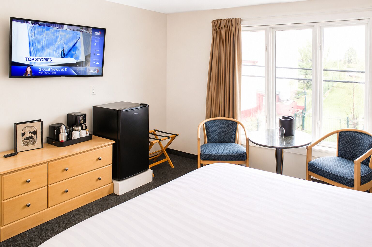 Ein Hotelzimmer mit einem Bett, einem Fernseher, der Nachrichten zeigt, einem Schreibtisch mit einer Kaffeemaschine und zwei Stühlen.