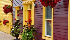 A yellow and purple house with hanging flower baskets and potted plants on the porch. - Rum Runner Inn (Lunenburg)