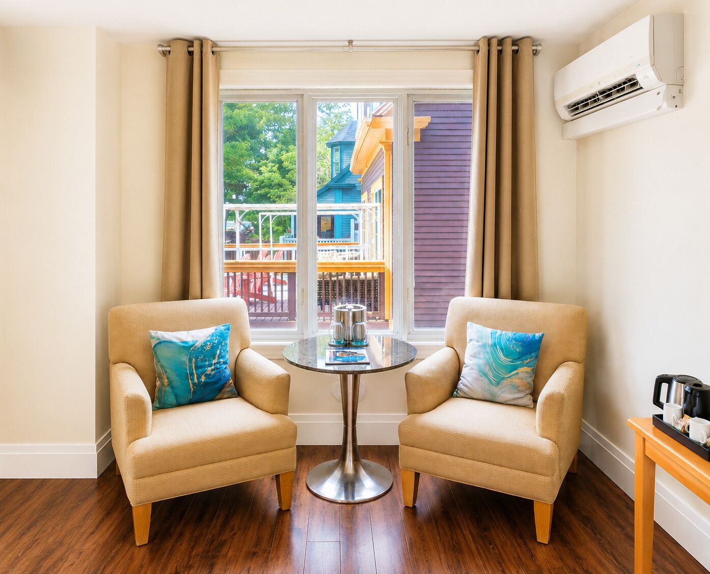 A room with two beige armchairs, a small round table, and a view of a colorful building outside.