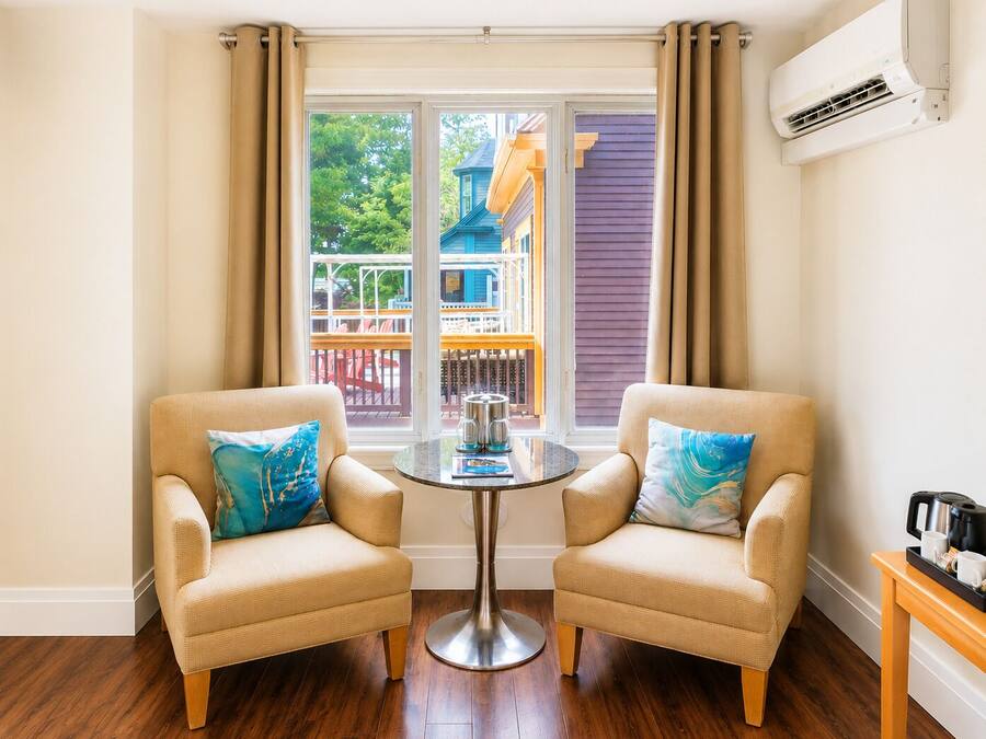 A room with two beige armchairs, a small round table, and a view of a colorful building outside.