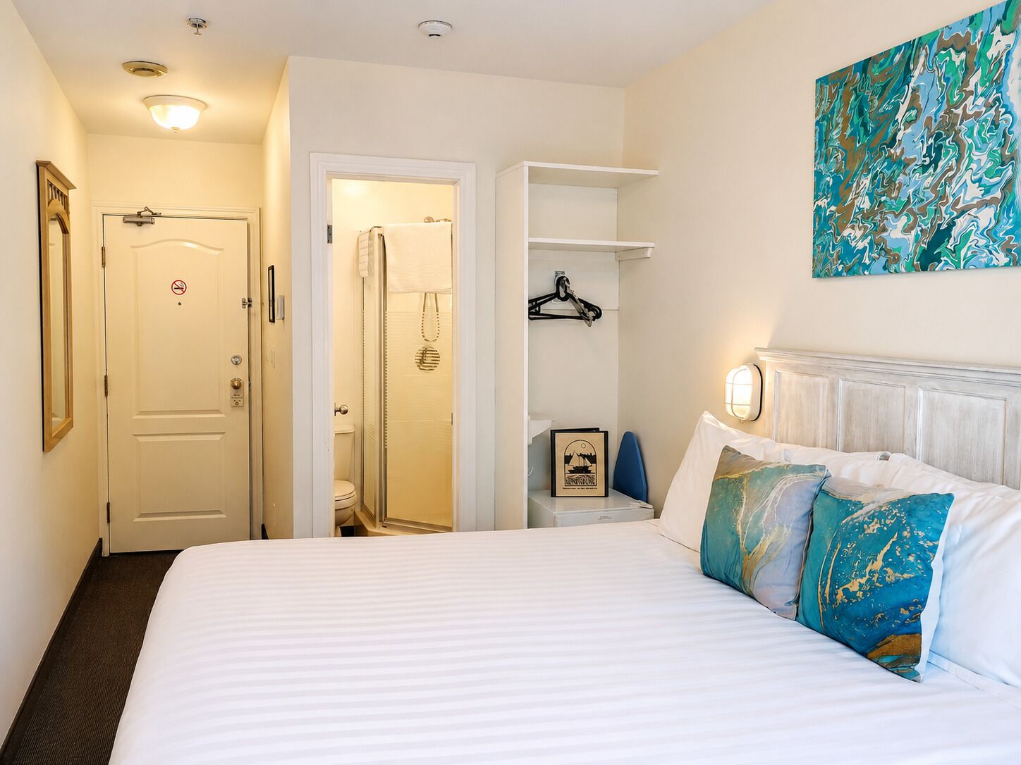 A hotel room with a bed, a bathroom, a coat rack, and a wall-mounted artwork.