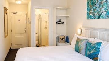 Habitación de hotel con cama, baño, perchero y una obra de arte colgada en la pared.