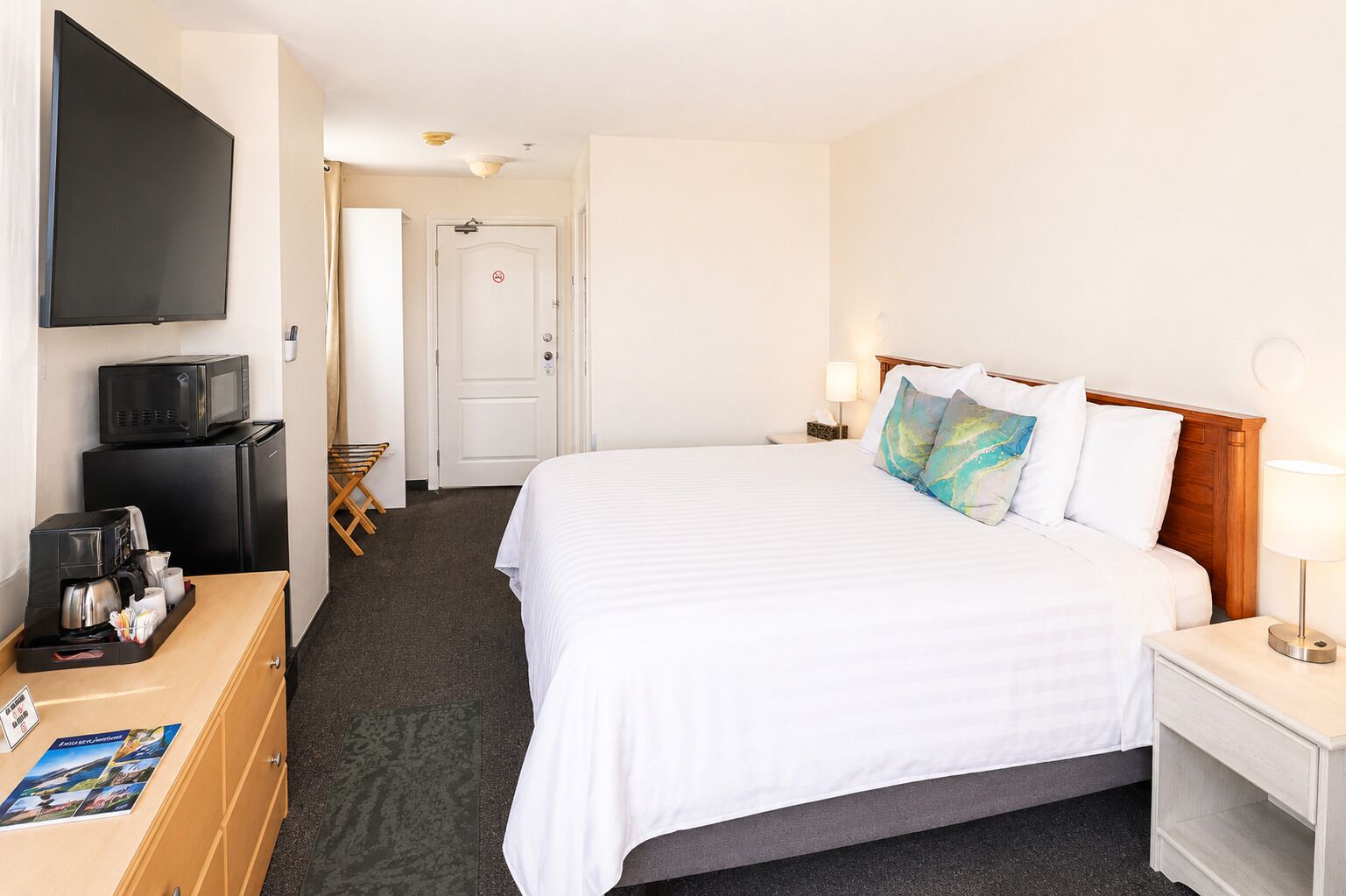 A hotel room with a bed, a TV, a desk with a coffee maker, and a door.