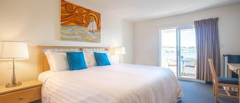 A hotel room with a bed, two bedside lamps, a painting, a chair, and a view of the outdoors.