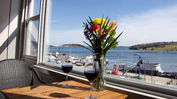 A table with two wine glasses and a vase of flowers by a window overlooking a harbor. - Rum Runner Inn (Lunenburg)