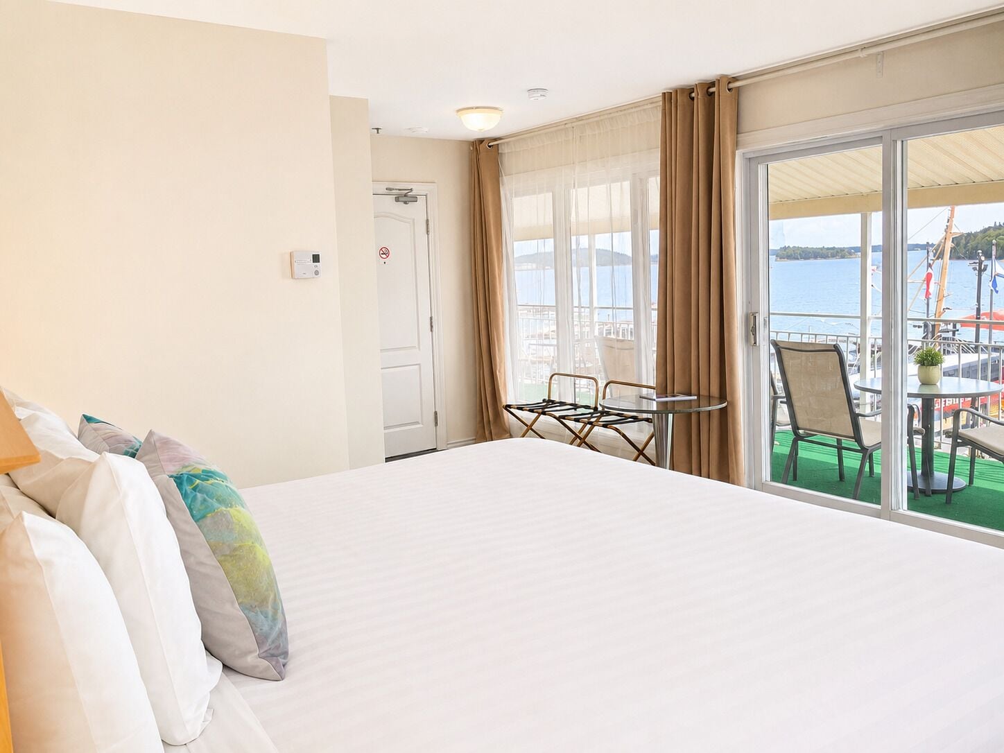 Quarto de hotel com cama, uma pequena mesa, cadeiras, vista para o mar e uma varanda com área de estar ao ar livre.