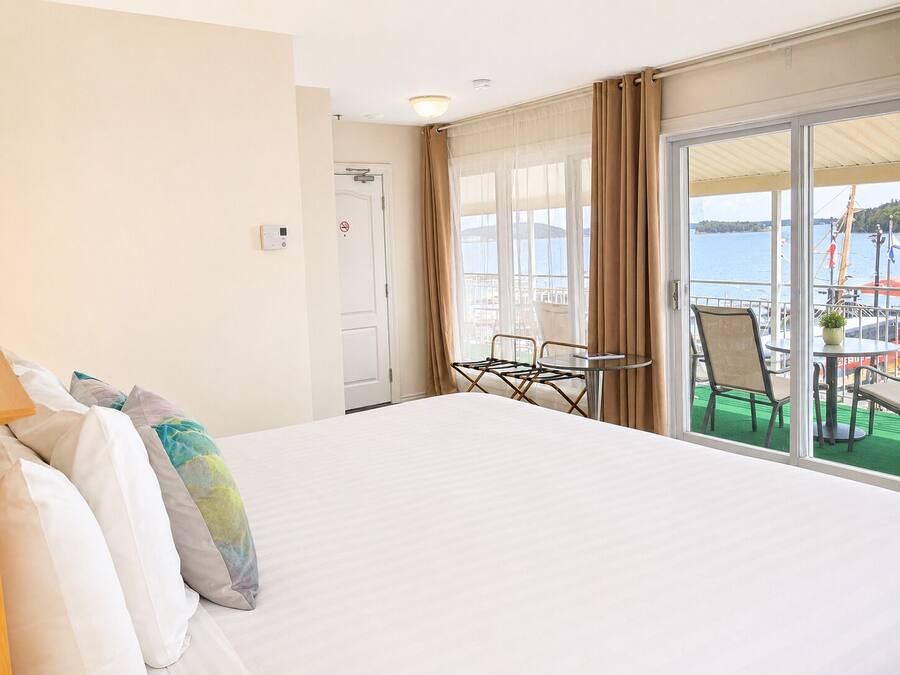 A hotel room with a bed, a small table, chairs, a view of the sea, and a balcony with outdoor seating.