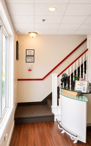 Zona de recepción de hotel con una escalera, un mostrador de vidrio y un cartel que indica la disponibilidad de habitaciones.