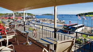 A covered outdoor seating area with tables and chairs, overlooking a harbor with boats and flags. - Rum Runner Inn (Lunenburg)