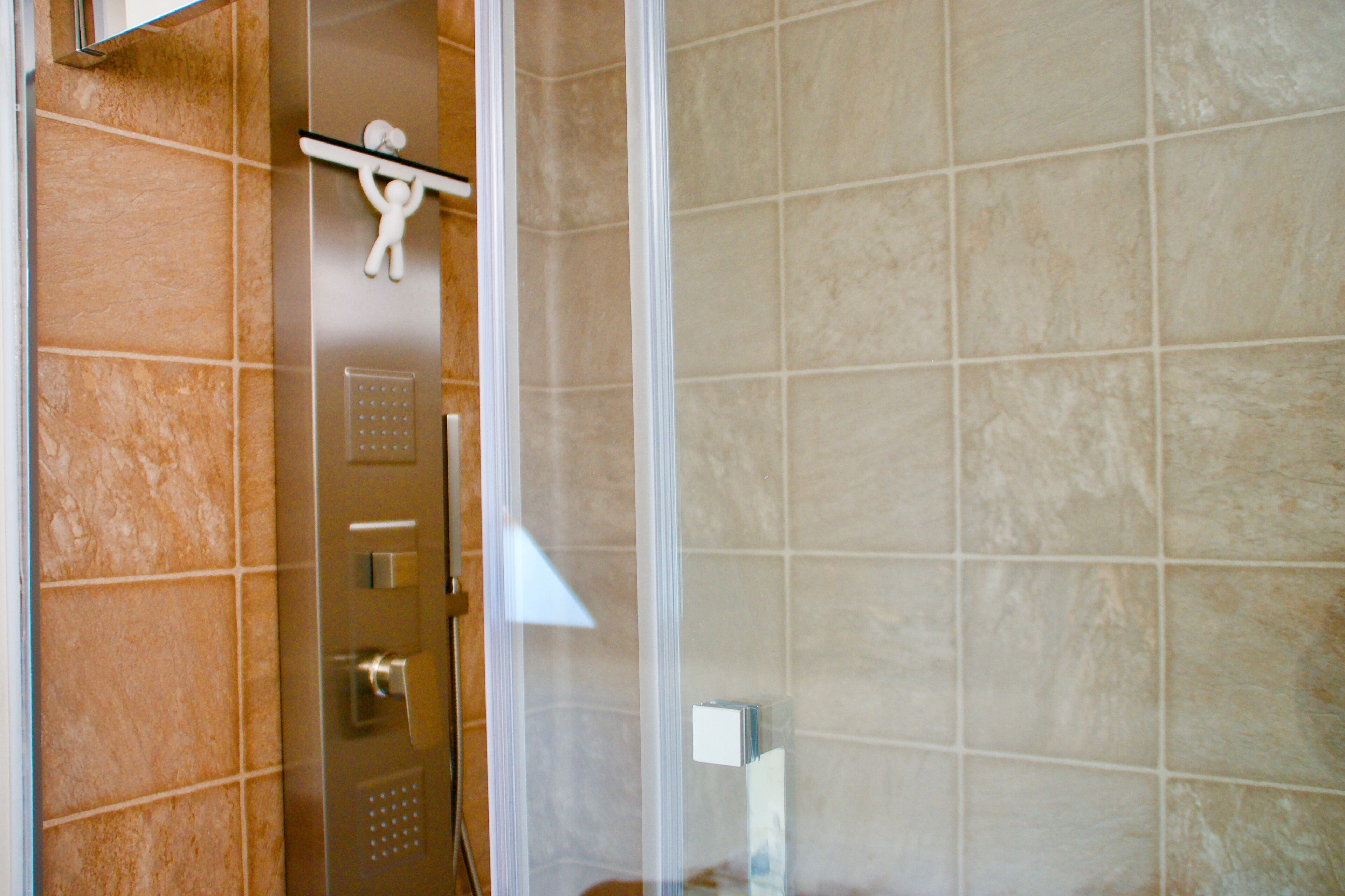 Un baño con baldosas color beige, una puerta de ducha y un perchero con una toalla.