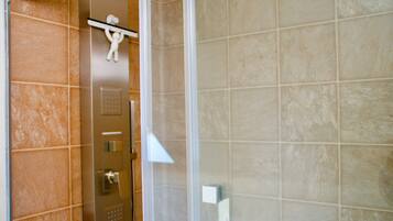 Un baño con baldosas color beige, una puerta de ducha y un perchero con una toalla.