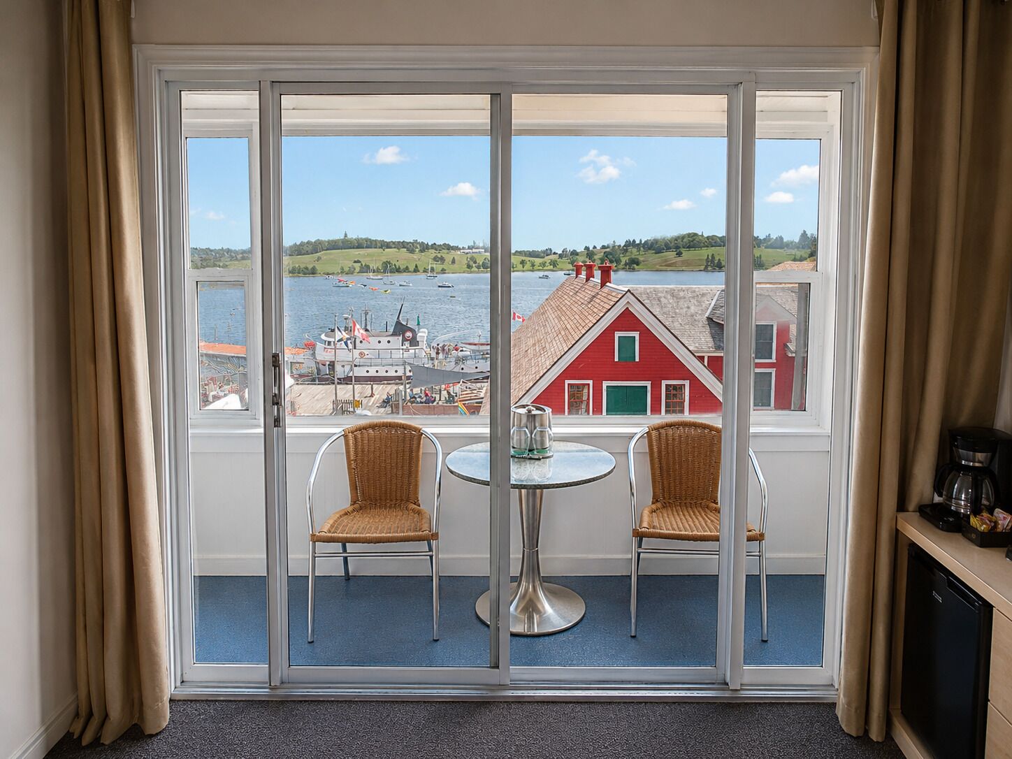 A room with a large sliding glass door, two wicker chairs, a small round table, and a coffee maker on a counter.