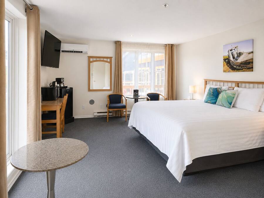 Une chambre d’hôtel comprenant un lit, un bureau, une chaise, une petite table, un téléviseur et une fenêtre avec des rideaux.