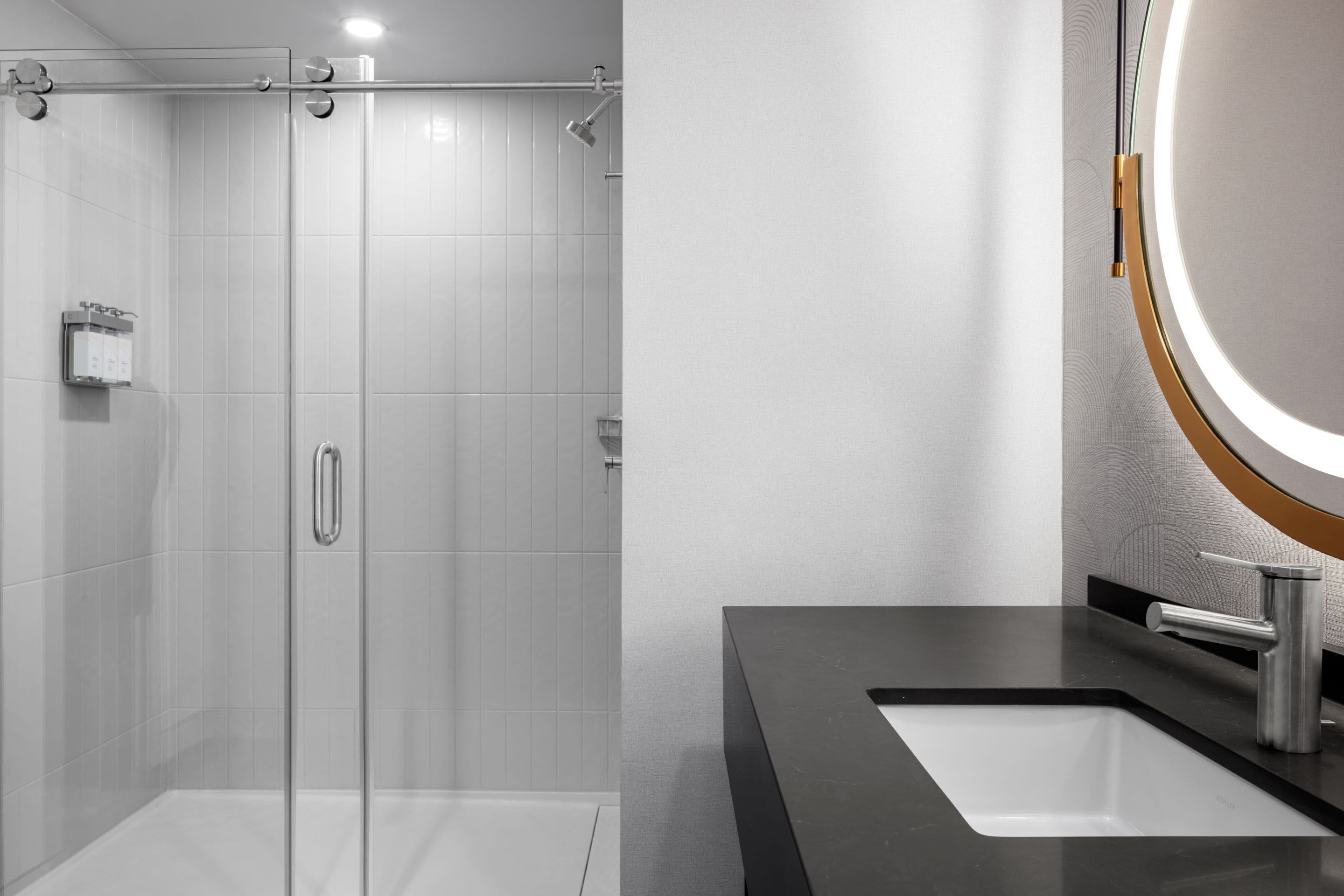 A modern bathroom with a glass-enclosed shower, a large mirror with a gold frame, and a black countertop with a white sink.