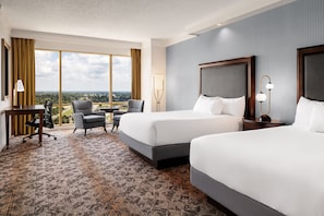 Habitación de hotel con dos camas, un escritorio, una silla y vistas a la ciudad.