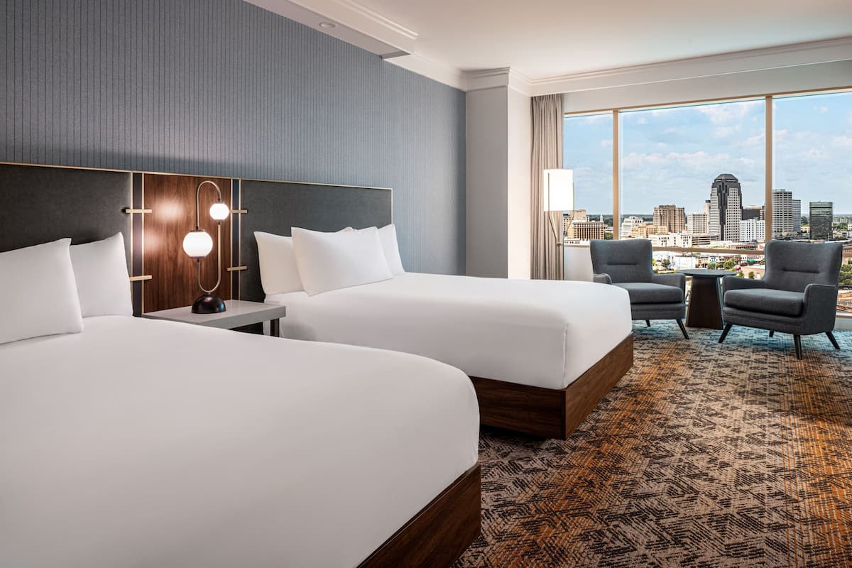 Habitación de hotel con dos camas, vista a la ciudad y alfombra estampada.