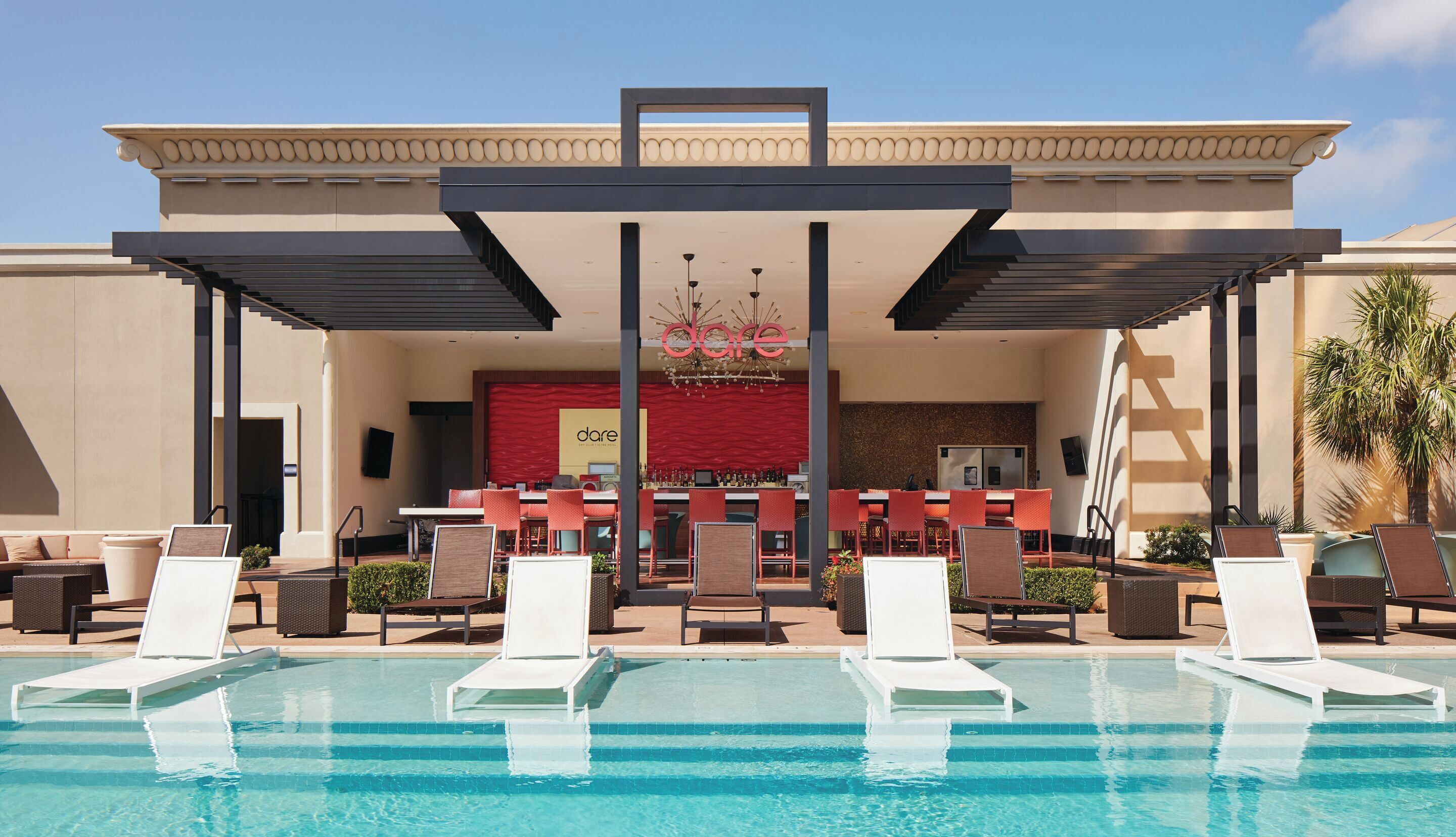 Zona de piscina de hotel con sillones reclinables, un bar y una piscina.