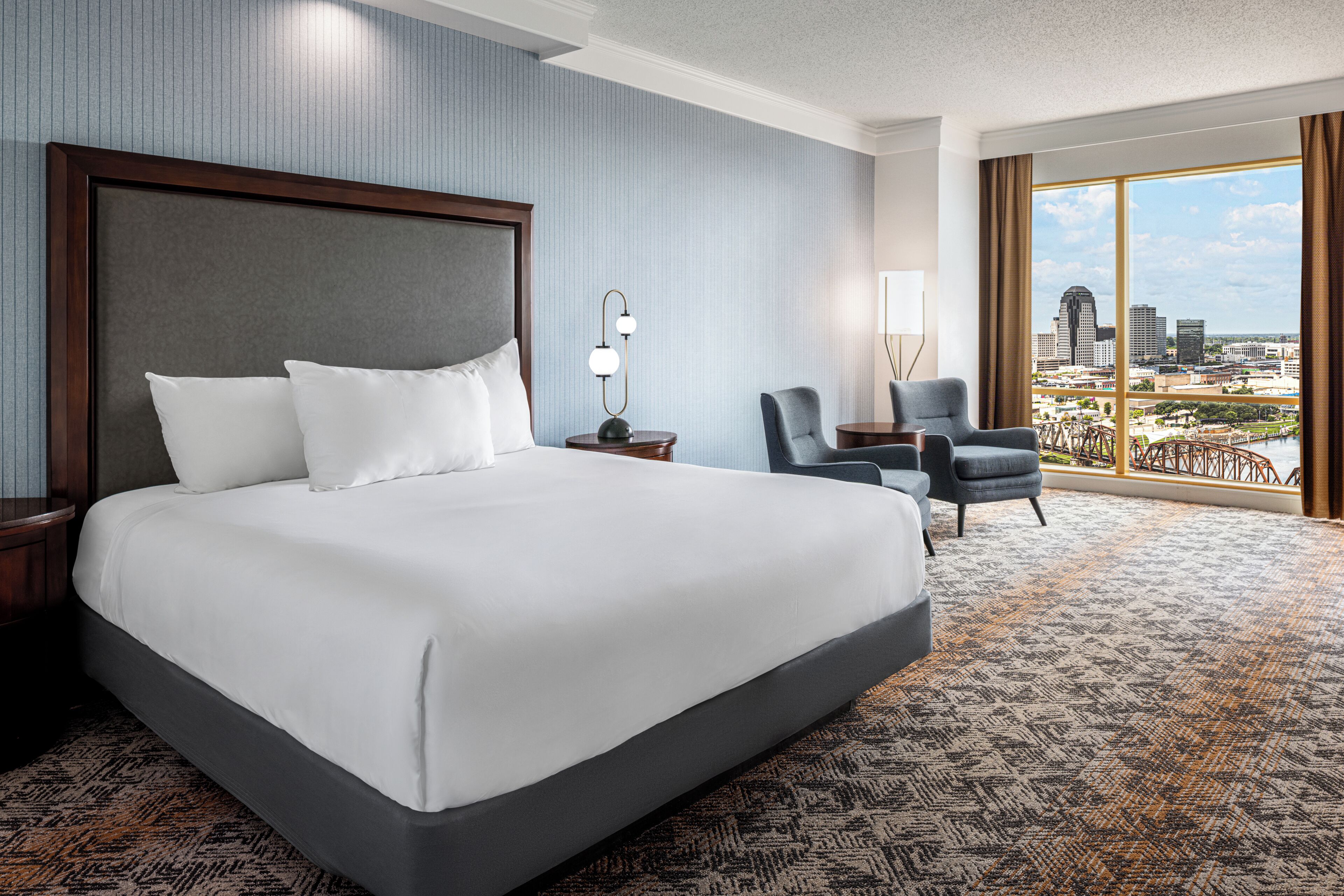 A hotel room with a large bed, a desk, a chair, and a view of the city.