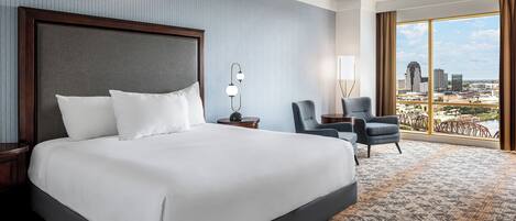 A hotel room with a large bed, a desk, a chair, and a view of the city.