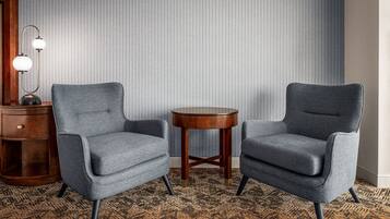 Deux fauteuils gris aux pieds en bois et une petite table en bois placée entre eux, le tout posé sur un tapis à motifs.