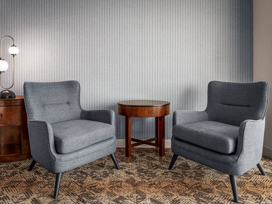 Deux fauteuils gris aux pieds en bois et une petite table en bois placée entre eux, le tout posé sur un tapis à motifs.