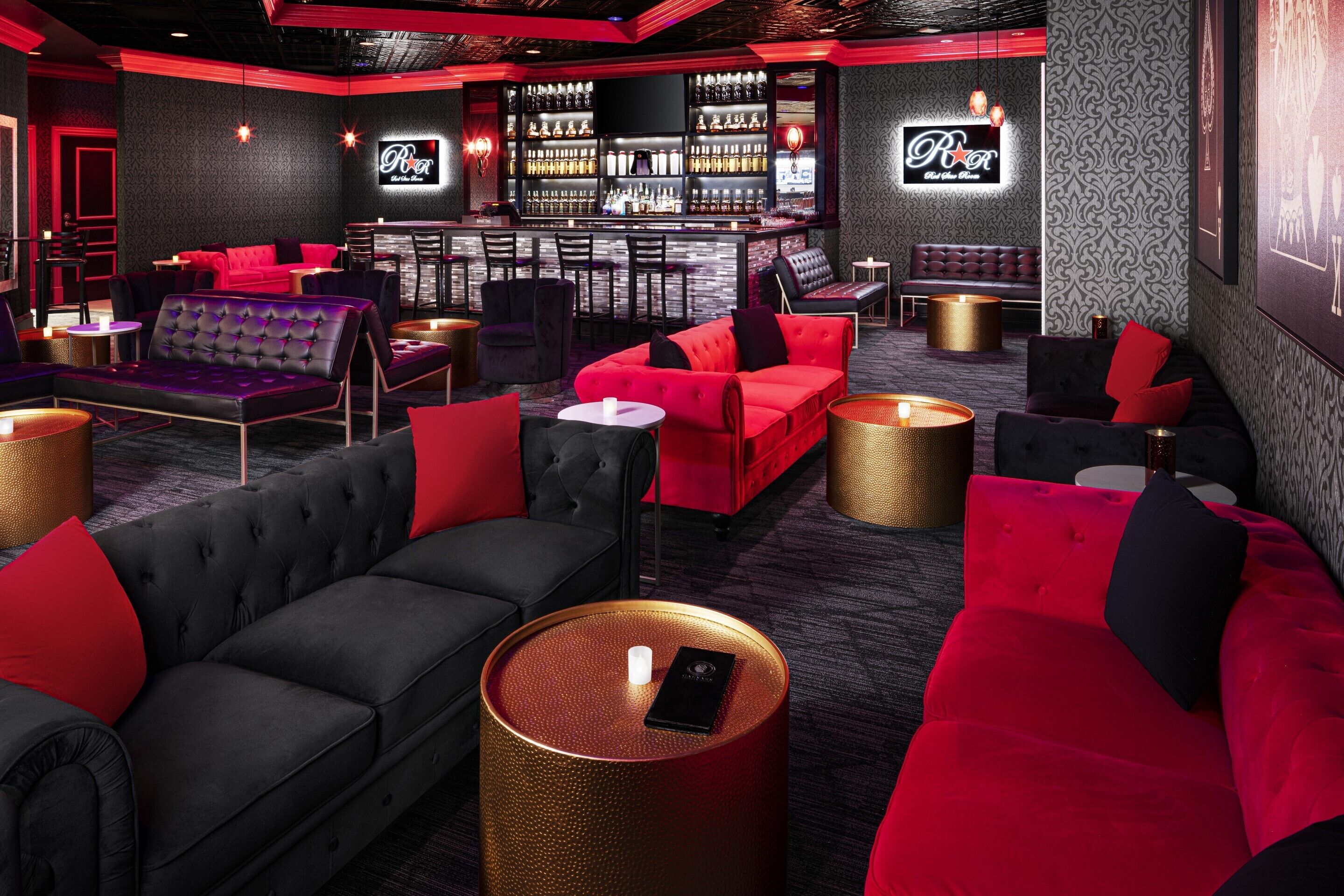 A bar area with red and black seating, a bar counter, and a neon sign.