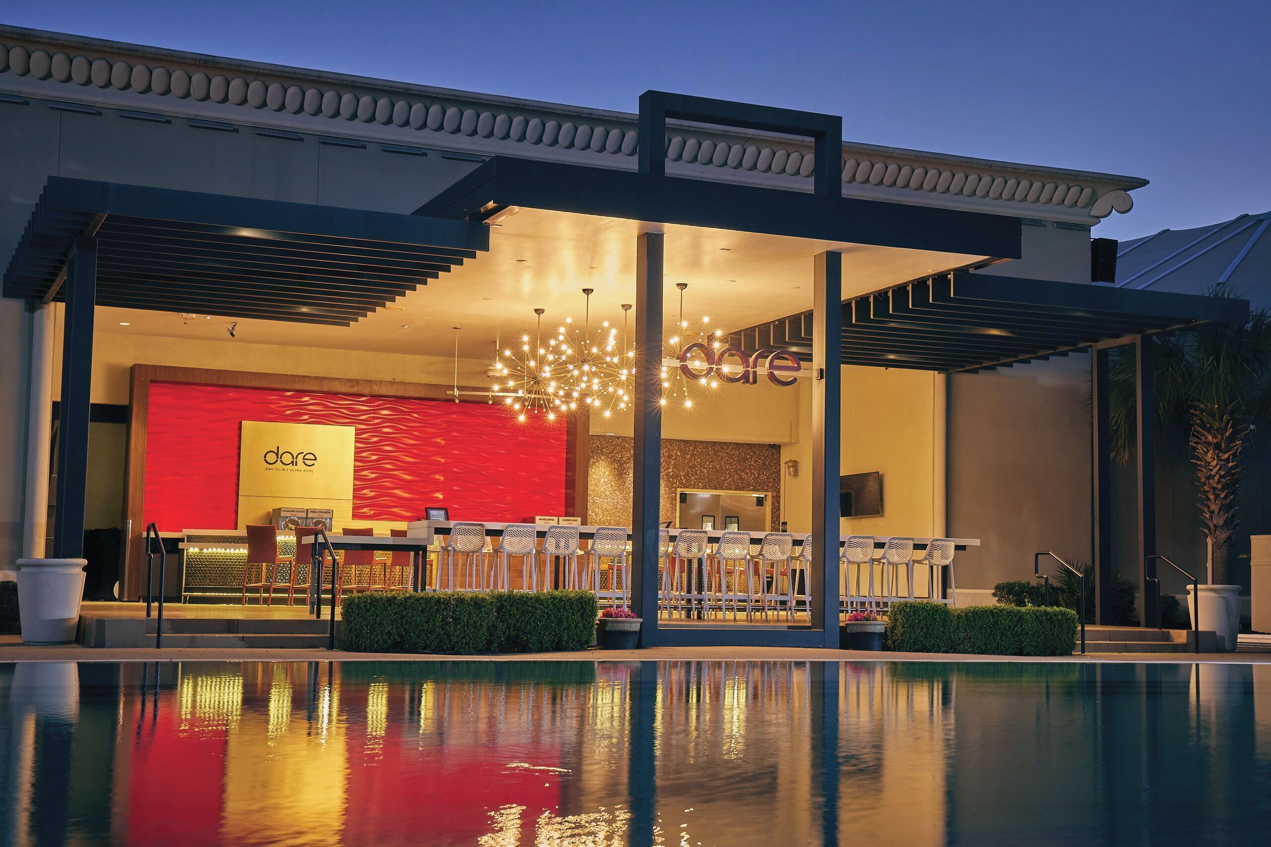 A modern hotel exterior with a pool, outdoor seating, and a 'dare' sign.