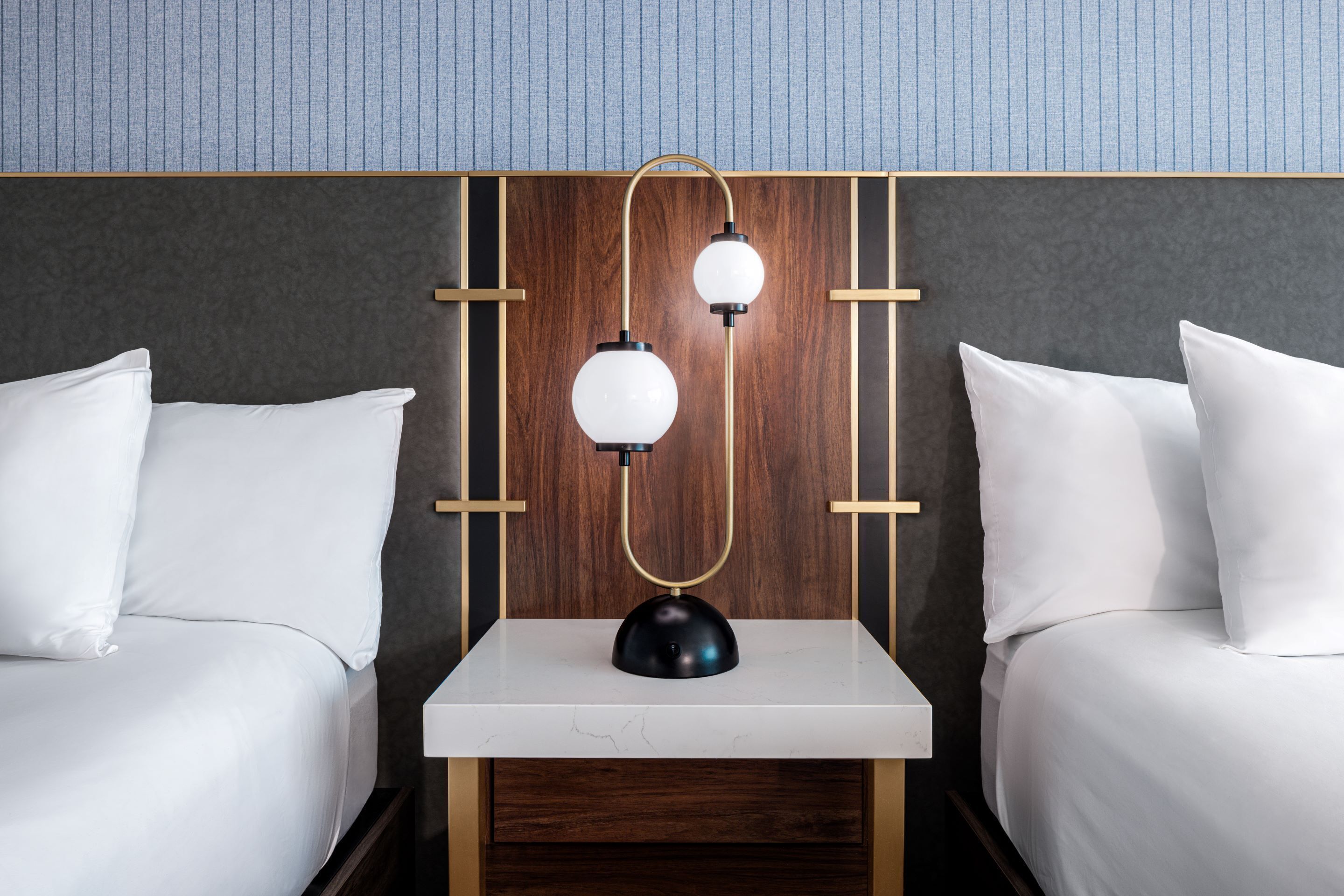 A hotel room with two beds, a bedside table, and a wall-mounted lamp.