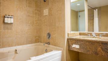 A bathroom with a bathtub, a sink with a granite countertop, and a mirror above the sink.