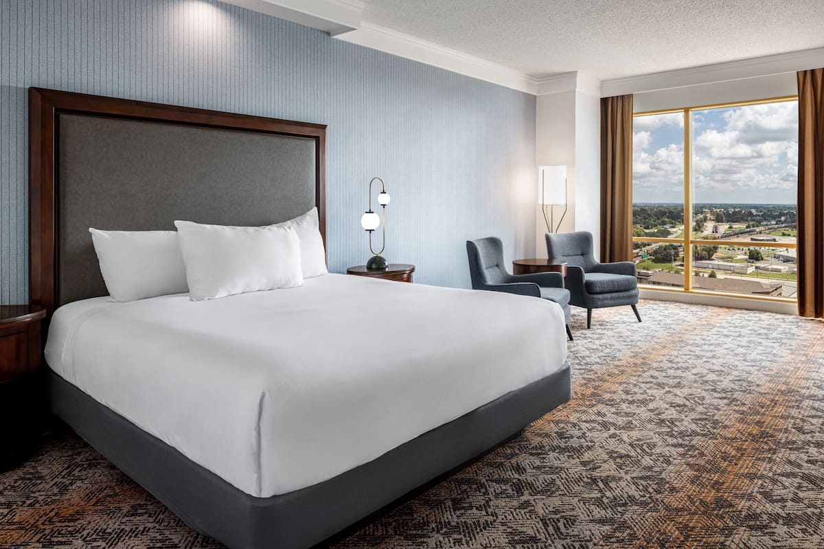 Habitación de hotel con una cama grande, una silla, un escritorio y vistas a la ciudad.