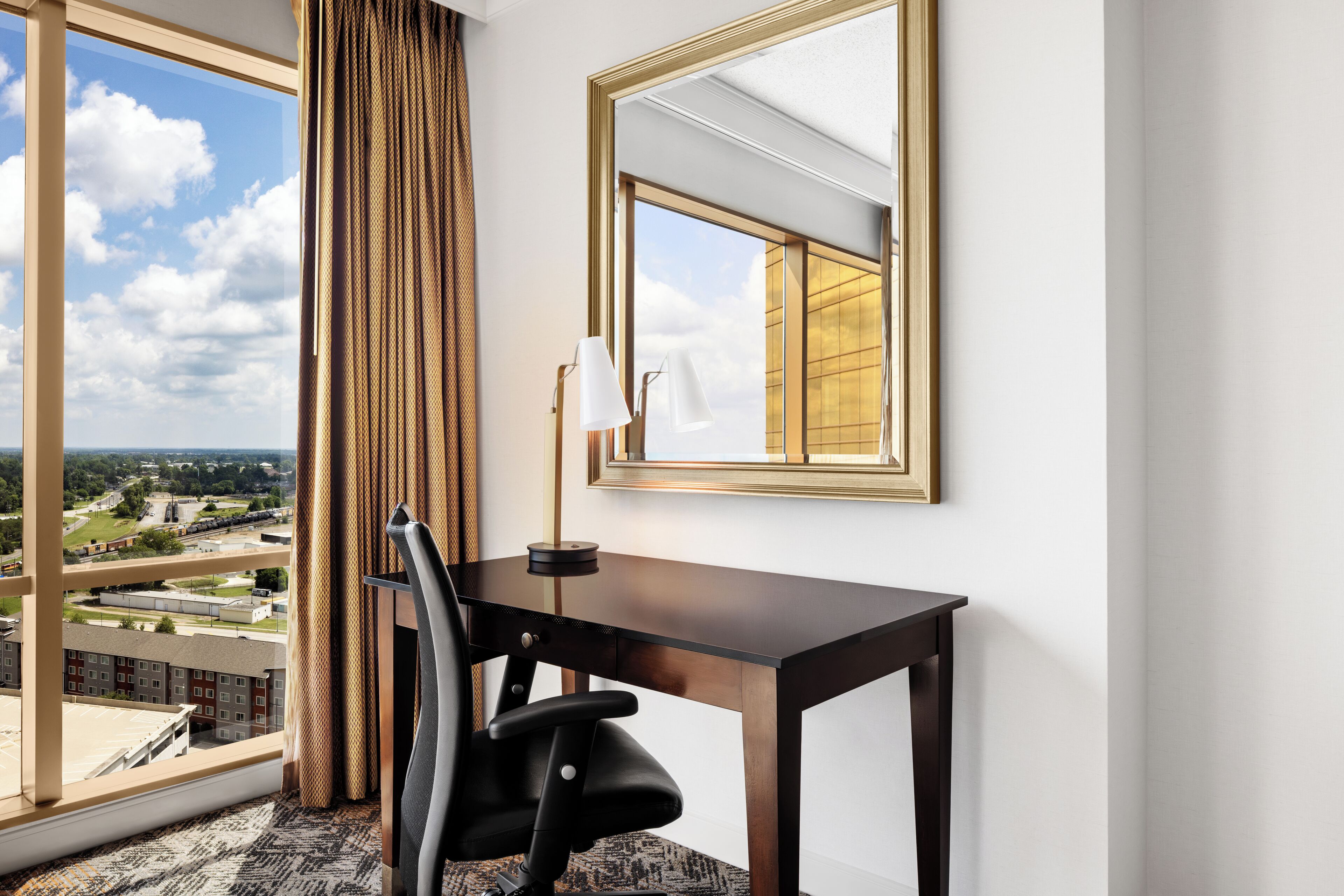 Una habitación de hotel con un ventanal grande, un escritorio, una silla y un espejo.