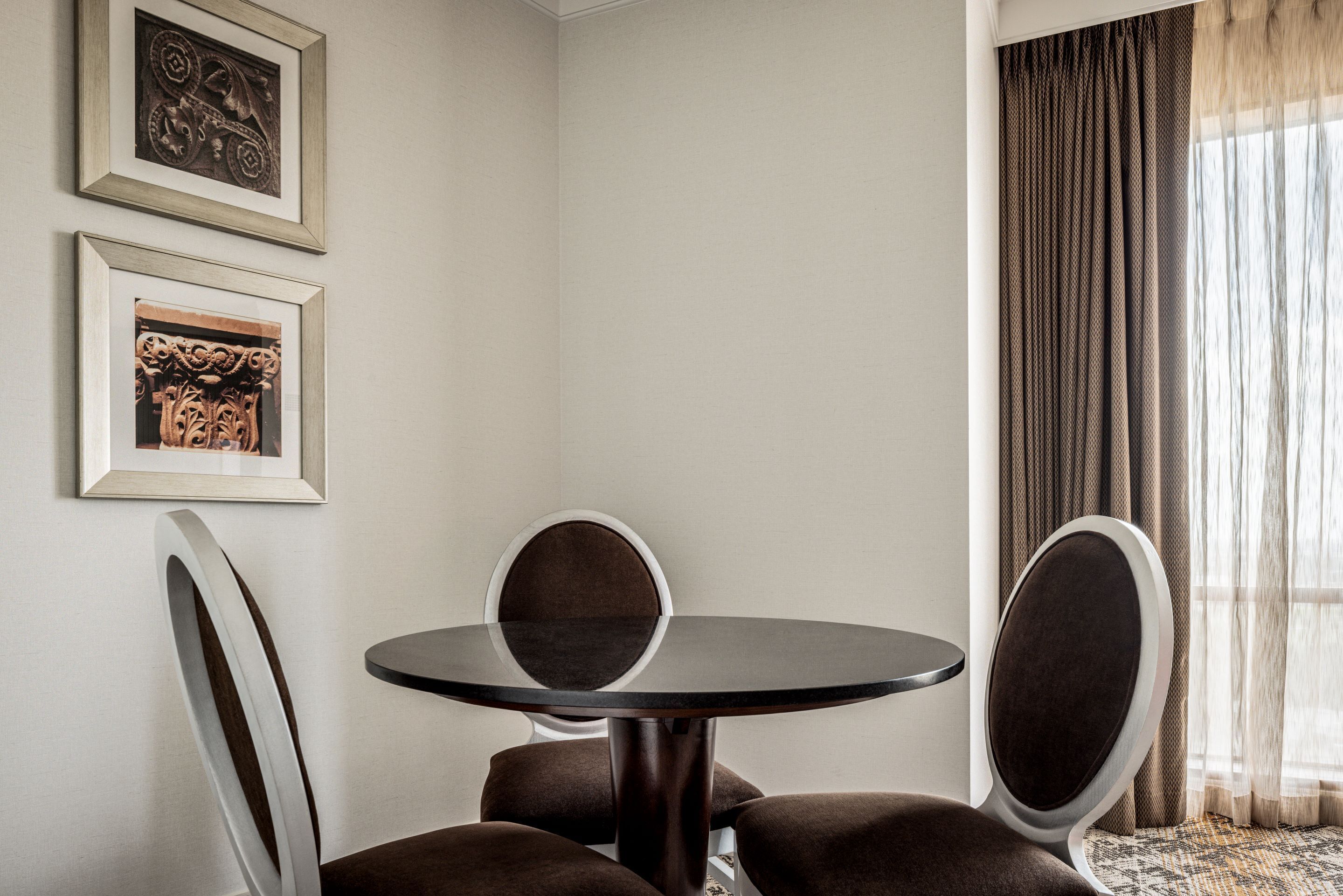 A room with a round table, two chairs, and two framed artworks on the wall.