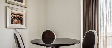 A room with a round table, two chairs, and two framed artworks on the wall.