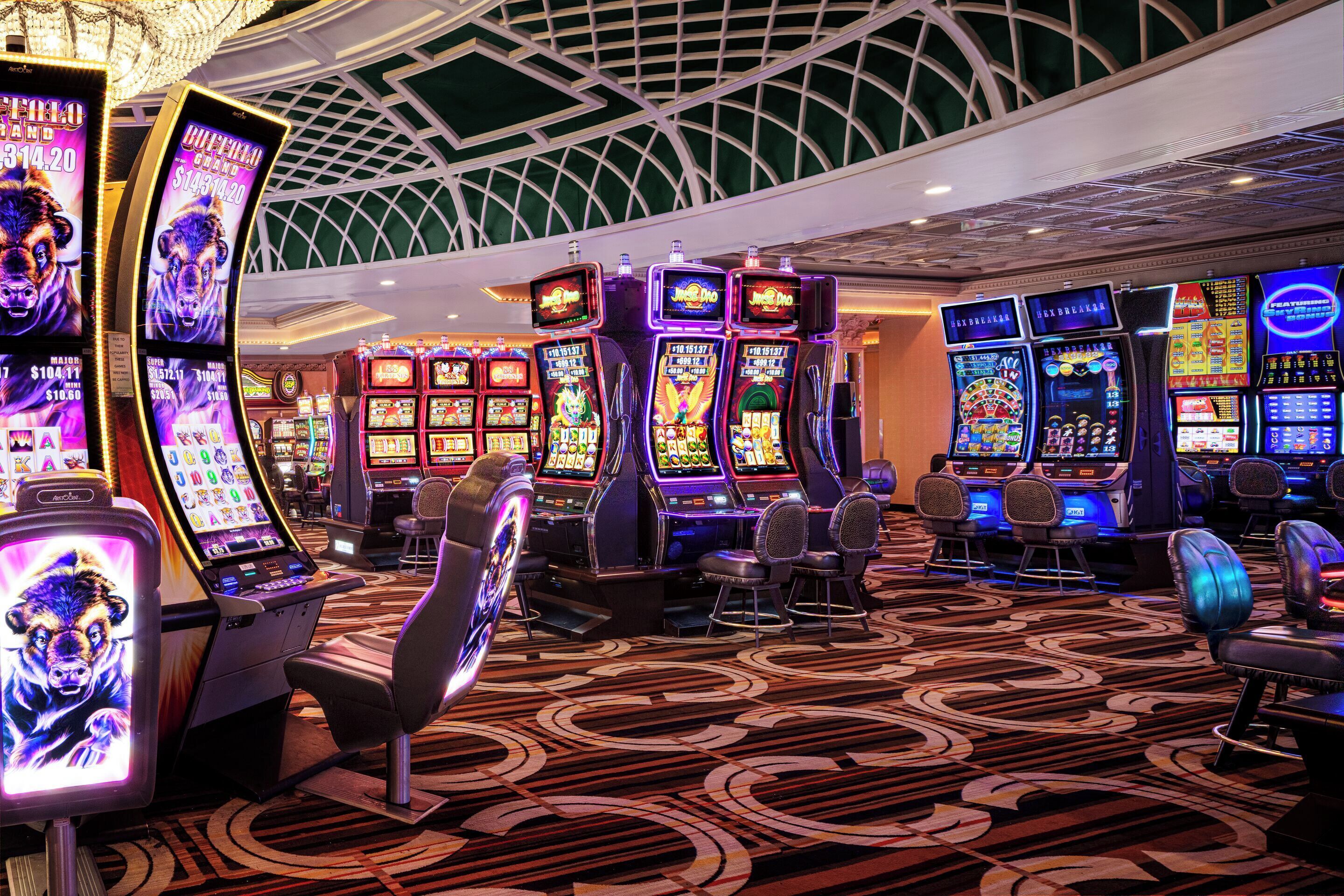 Un casino con máquinas tragamonedas y mesas de juego, una alfombra estampada y un diseño de techo llamativo.