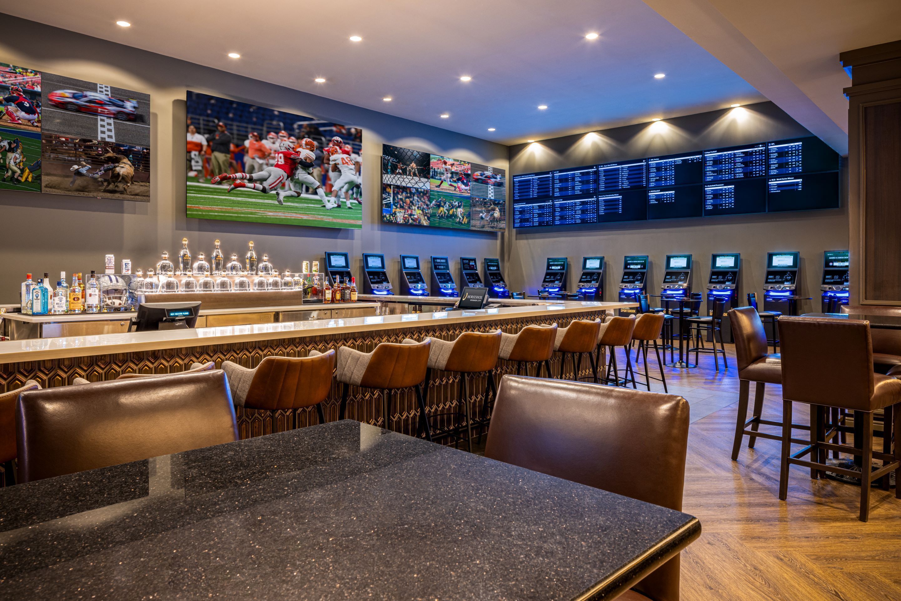 Un espace bar doté de plusieurs écrans diffusant des événements sportifs, un comptoir de bar avec des bouteilles et différents types de sièges.