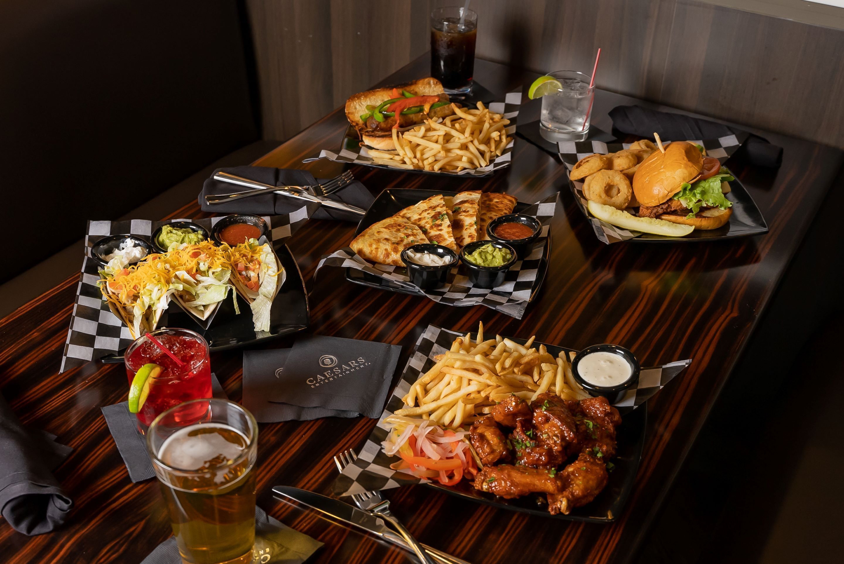 A dining table with various food items and drinks, including a burger, fries, chicken wings, and a salad.
