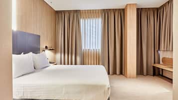A hotel room with a large bed, a wooden headboard, a nightstand, a desk, and a window with curtains.