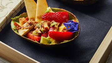 Two bowls of fruit salad with a decorative flower, placed on a dark cloth inside a wooden box.