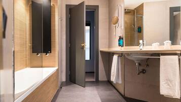 Un baño moderno con bañera acristalada, un espejo grande y un tocador con lavabo y toallero.