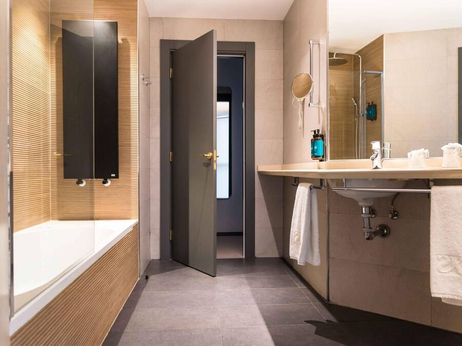 Un baño moderno con bañera acristalada, un espejo grande y un tocador con lavabo y toallero.