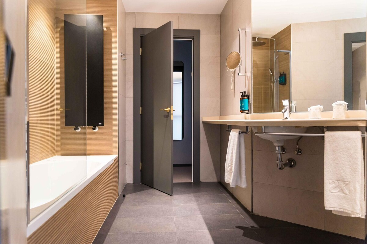 A modern bathroom with a glass-enclosed bathtub, a large mirror, and a vanity with a sink and towel rack.