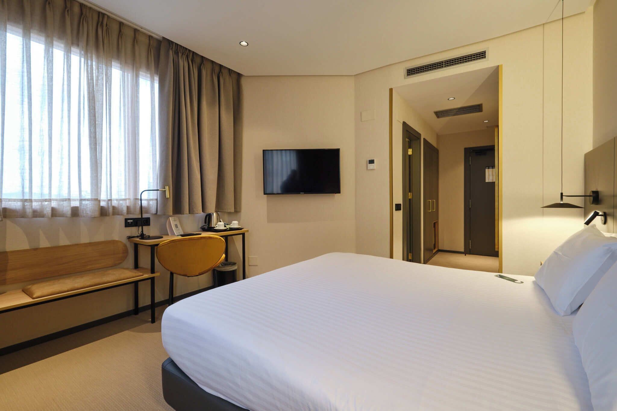 Habitació d'hotel amb un llit gran, una taula de treball amb una cadira, una televisió i un armari.